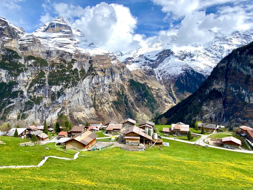 Kleines Schweizer Bergdorf auf grüner Blumenwiese vor imposanter Felswand im Lauterbrunnental