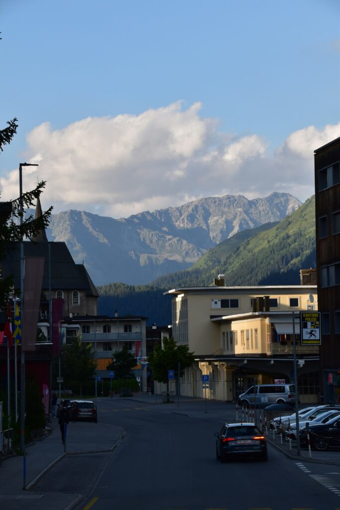 Straßenzug in einer Bergstadt mit Blick auf schroffe Alpengipfel im Hintergrund
