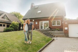 Ehepaar vor Einfamilienhaus im Garten – Symbol für Eigenheim und Immobilienkauf