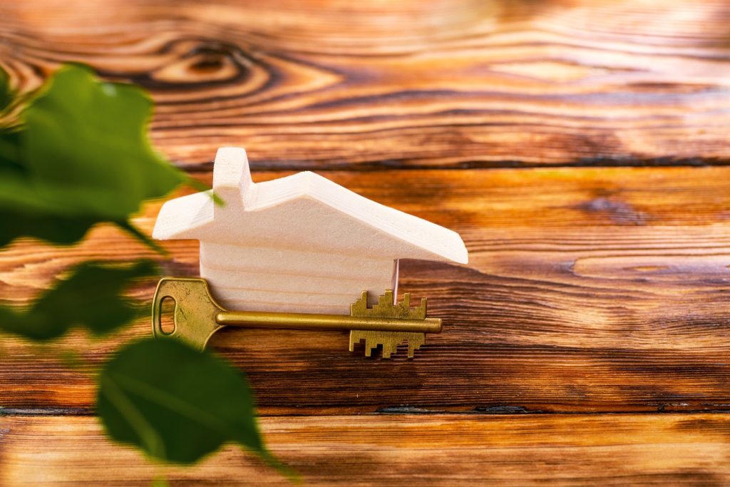 Holzhaus mit Schlüssel auf Holztisch – Symbol für Hauskauf und Immobilienbesitz